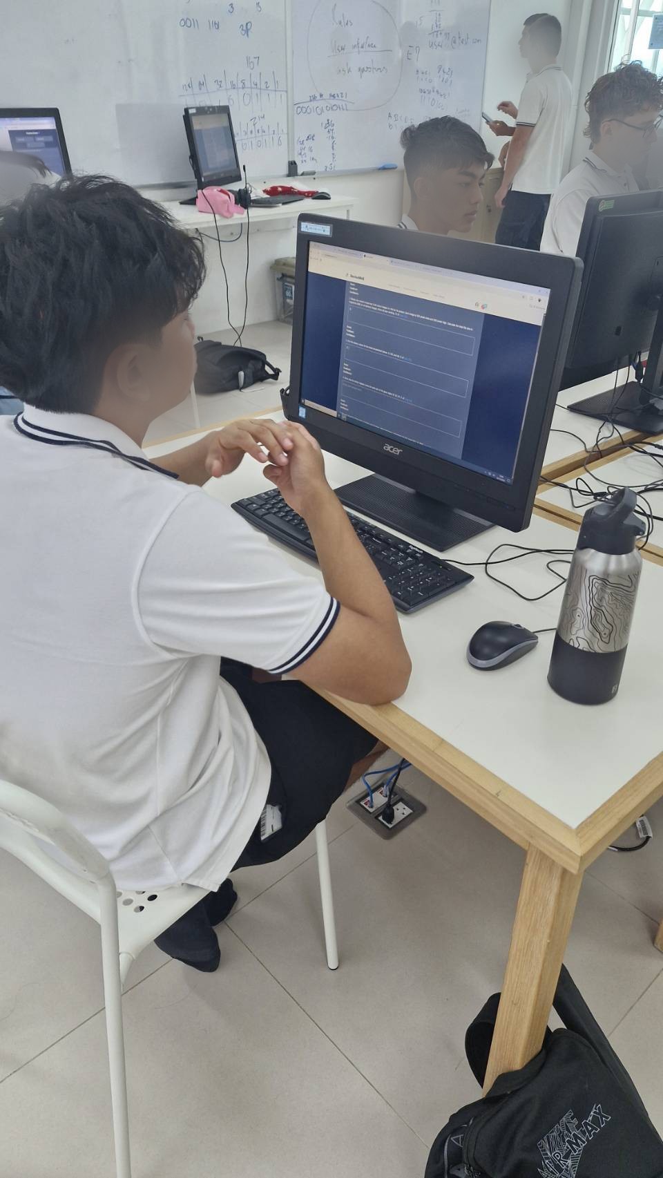 A student working through ReviseWell exam questions on a classroom computer. Face blurred for privacy.